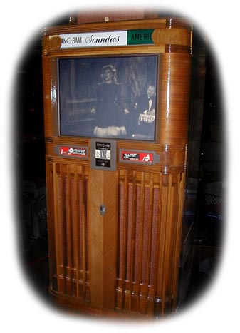 This is a Mills Panoram. This fantastic machine was first produced in 1939 by the Mills Novelty Company of Chicago, Illinois. The fabulous wood cabinetry houses a 16mm projector that plays special continuous loop films (Soundies) that typically show jazz and other musicians of the day.